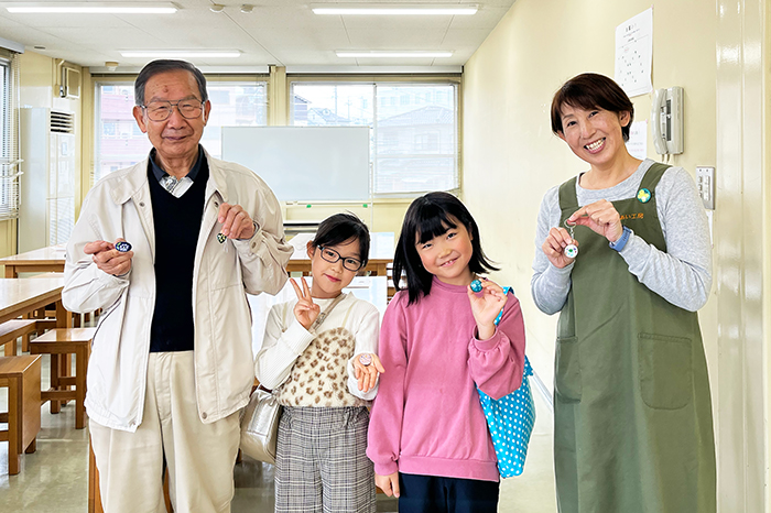 講師と参加者が七宝焼きを手に取って並んでいる写真