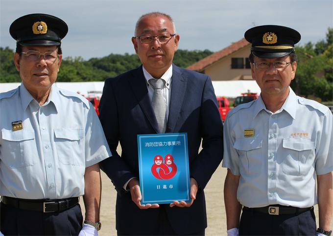 交付式にて日進市消防団協力事業所表示証を持つ株式会社スギ薬局様と消防団の方たちの写真