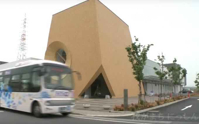 茶色の壁に三角の出入口に丸い大きな窓のついた、個性的な外観の日進市立図書館の写真