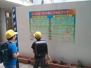 こうじしつもんコーナーの掲示を見ている、ランドセルを背負って黄色い帽子をかぶった男子生徒2人の写真