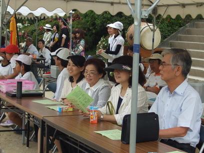 机を前に椅子に座って観戦する女性3名と男性1名の写真