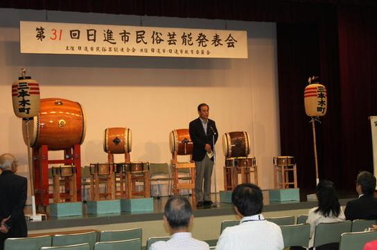 民俗芸能発表会にて壇上でたいこに囲まれている中、教育長があいさつをしている様子の写真
