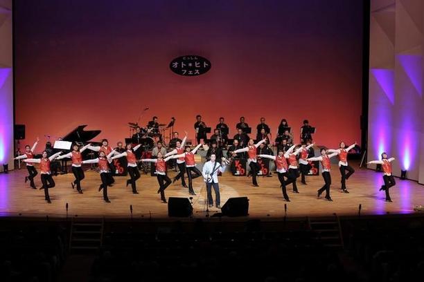 三味線を演奏する男性の後ろで複数名が踊りを踊っている写真
