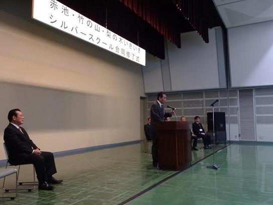日進市民会館にて赤池・竹の山・梨の木いきいきシルバースクールの合同修了式が行われ演説している写真