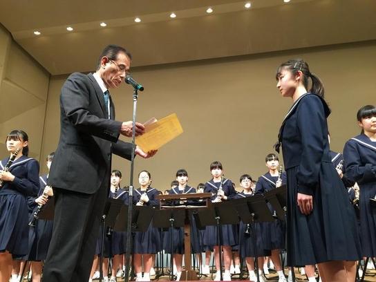 日進市民会館にて開催された日進西中学校吹奏楽部定期演奏会において、壇上にて教育長より表彰状を授与している様子の写真