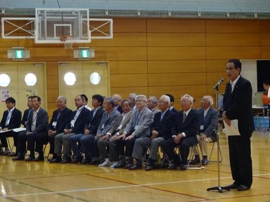 日進市スポーツセンターにて日進市少年少女発明クラブの企画運営員会及び開講式が行われた際に演説している男性の横で数名の出席者が座っている様子の写真