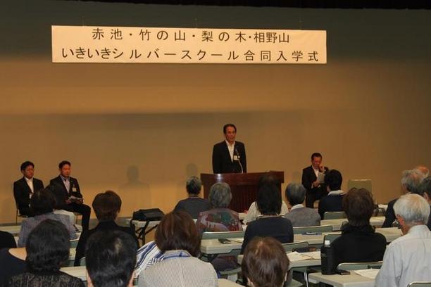 日進市民会館にて赤池・竹の山・梨の木・相野山いきいきシルバースクール合同入学式が行われ際に壇上で演説をしている様子の写真