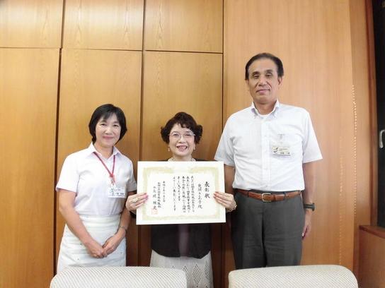 前日進市図書館協議会委員の鬼頭さゑ子氏へ、全国公共図書館協議会からの表彰状を授与した際の集合写真、真ん中に受賞者、左に女性、右に男性