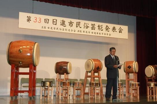 日進市民会館にて第33回民俗芸能発表会が開催され、教育長と教育委員が出席し太鼓に囲まれたなか演説している様子の写真
