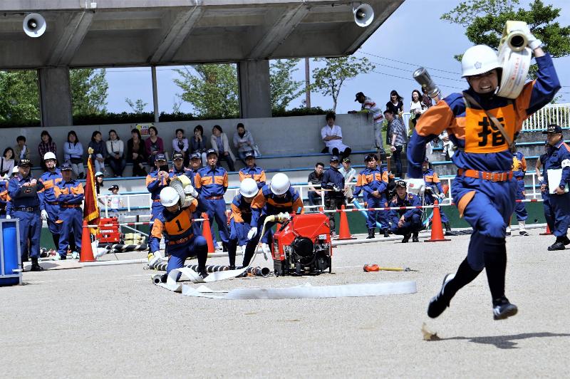 開始の合図とともに標的に向かってホースを運ぶ団員＝日進市総合運動公園で