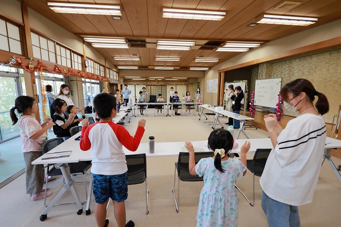 子どもと学生がみんなで手遊びをしている写真