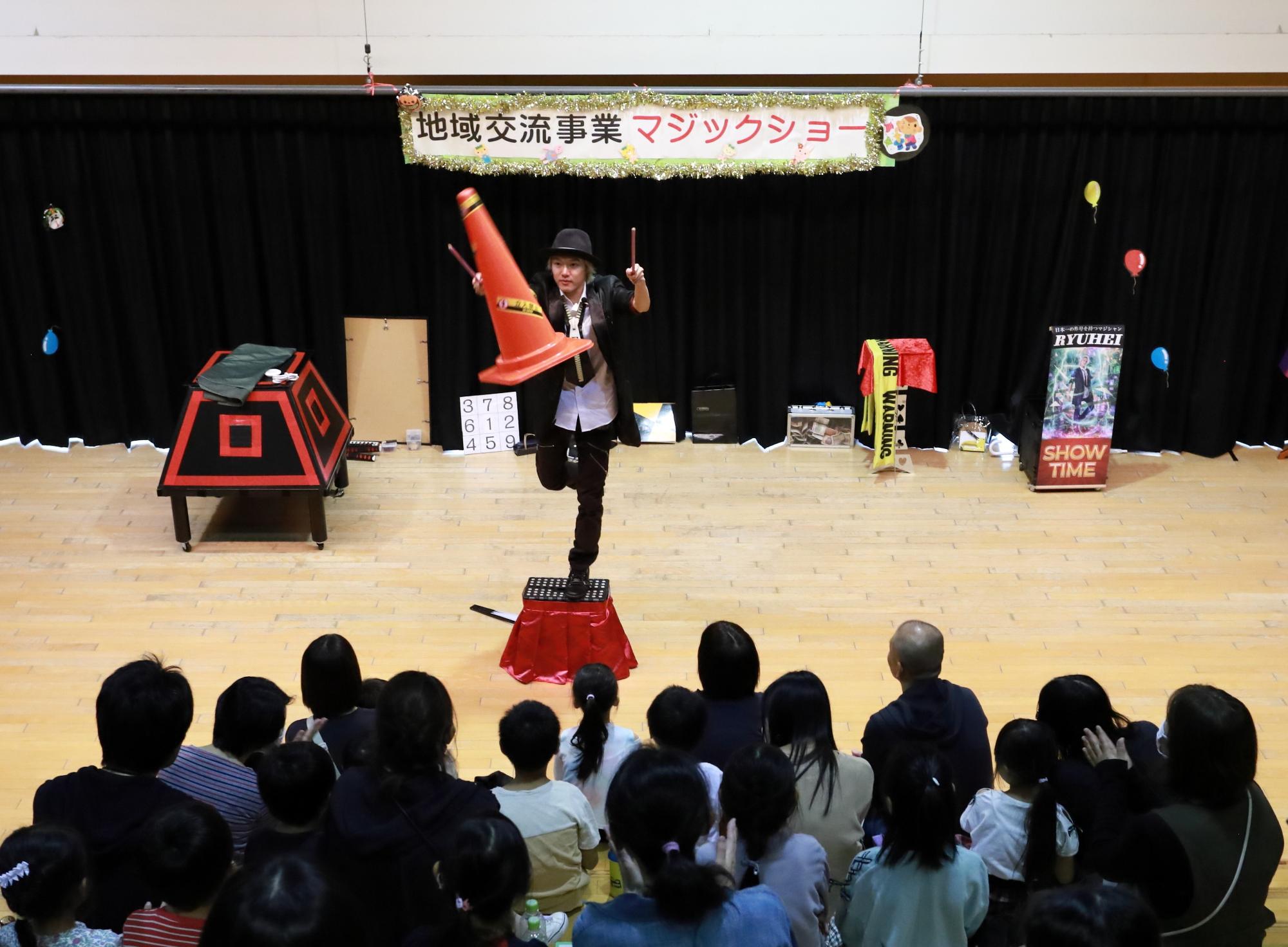マジシャンの中村龍平さんが踏み台の上でパイロンを手を触れずに宙に浮かしている写真