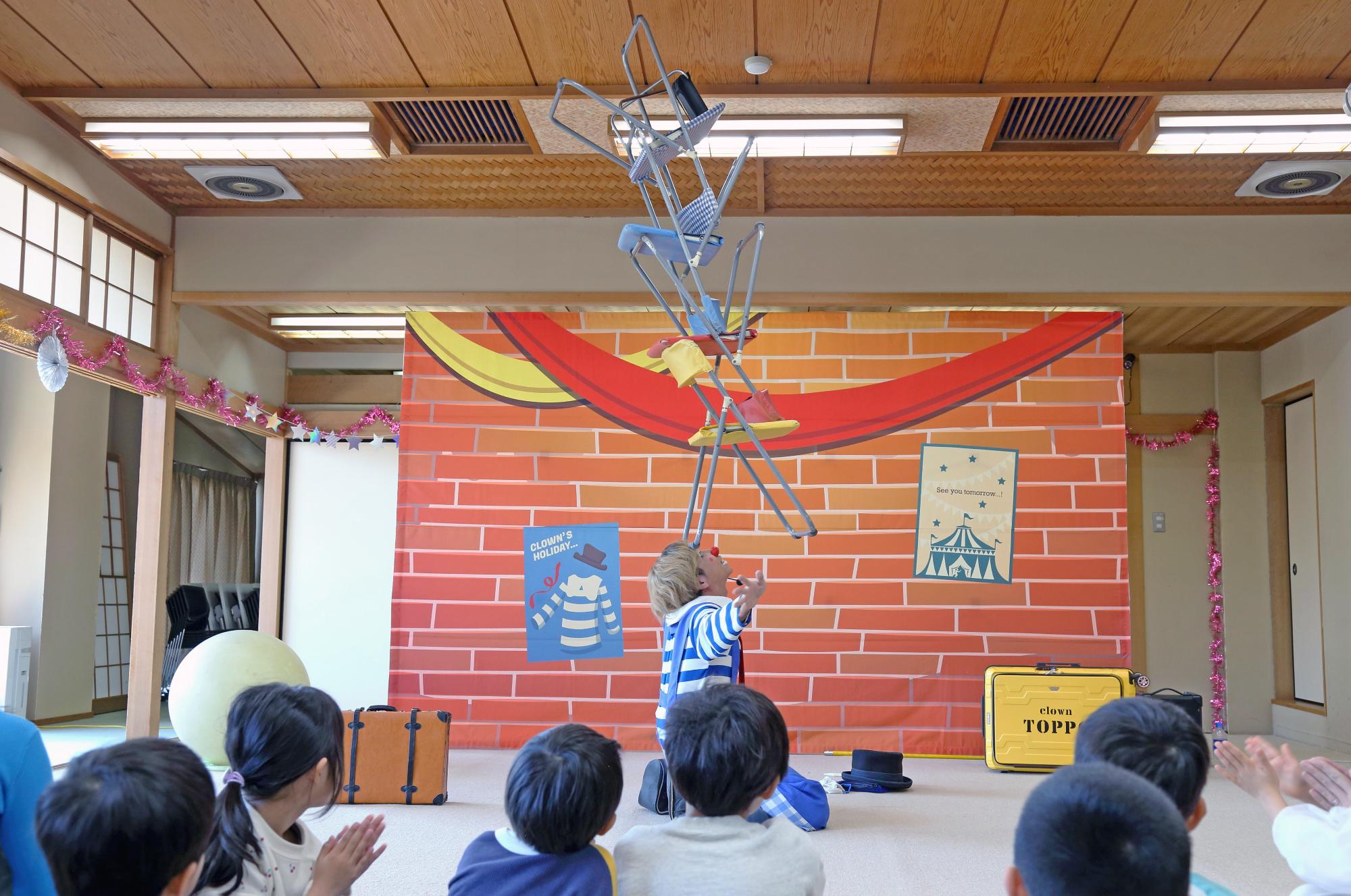 額の上にたくさんの椅子を積み重ねるピエロの写真