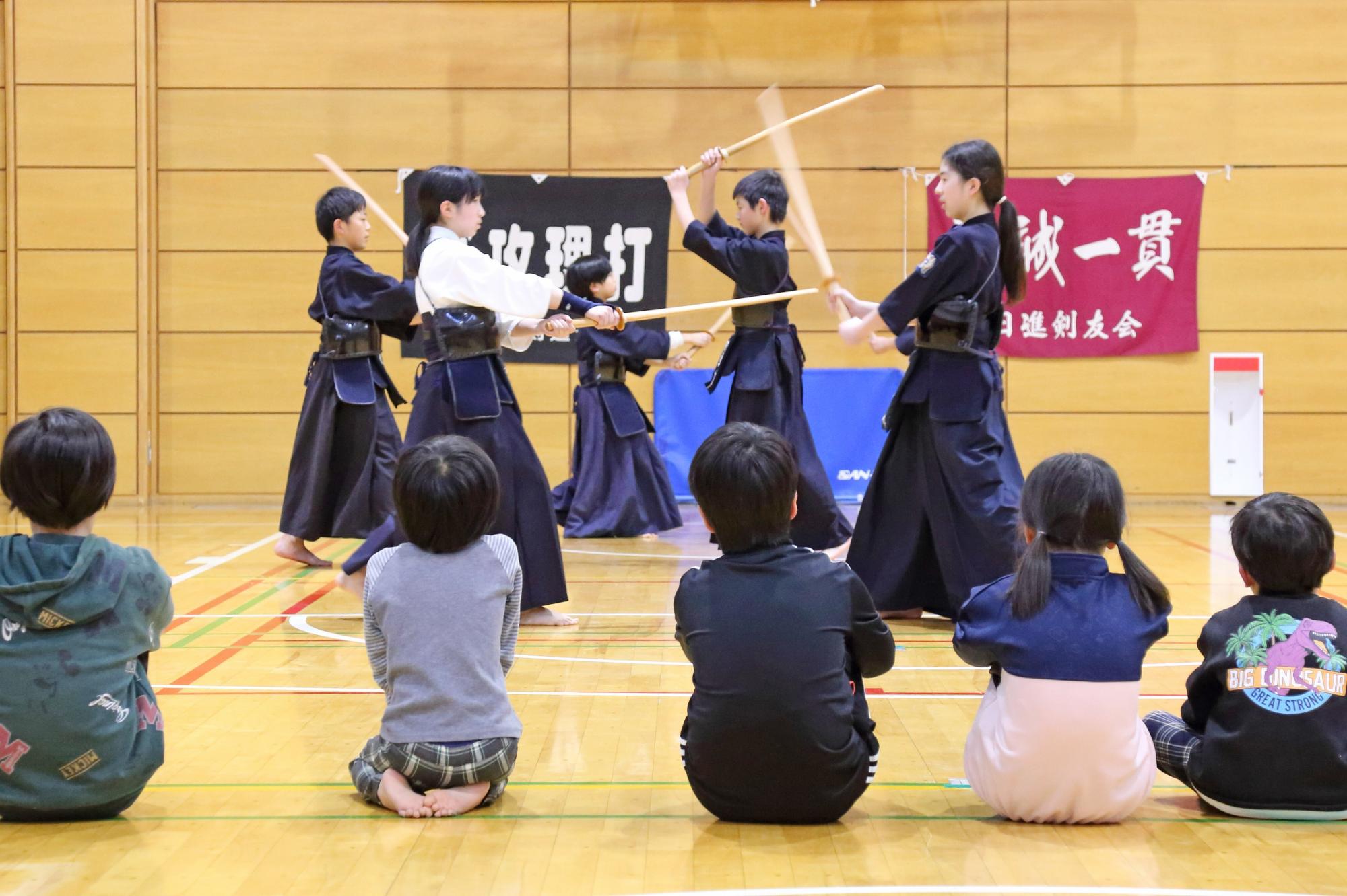 会員剣士による基本技の実演をみる参加者の後ろ姿の写真