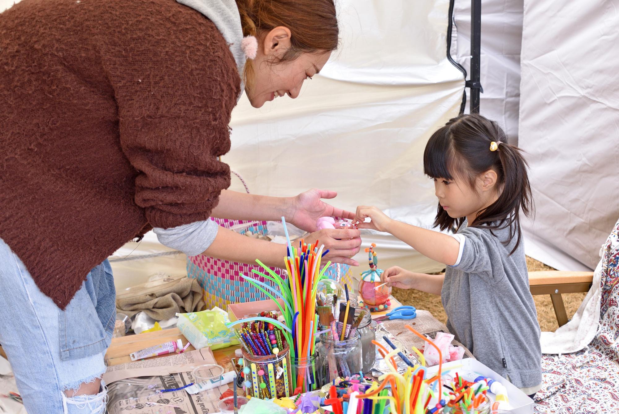 スタッフに手伝ってもらいながら手作りのアクセサリーを作るこどもの写真