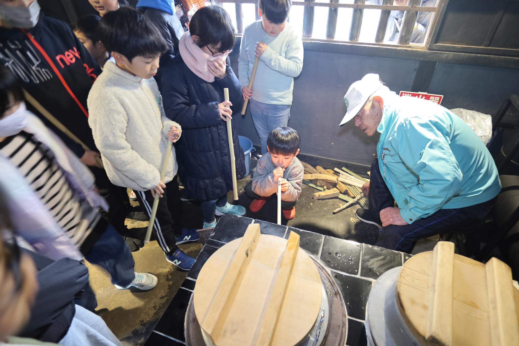 火吹き竹を吹いて釜の火を起こす子どもの写真