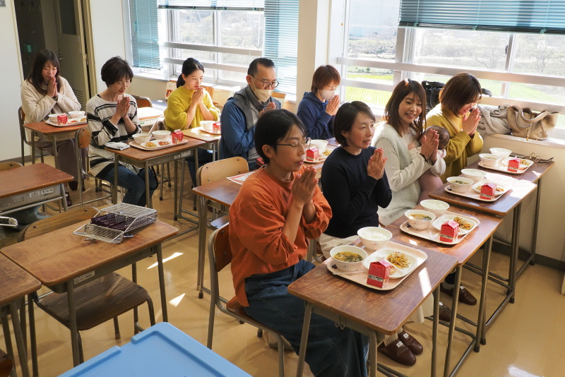 参加者が学習机に座って給食を前にいただきますをする写真