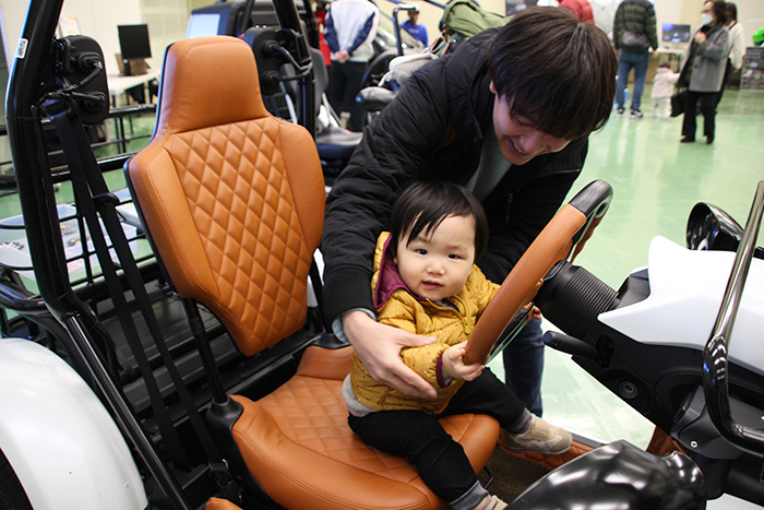 展示されている1人乗り電気自動車に座りハンドルに手を添える子どもと親の写真