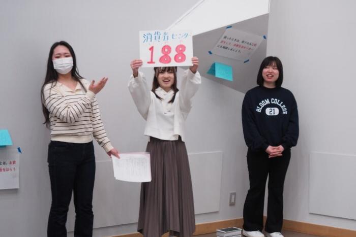 「消費生活センター 188」と書かれた紙を掲げる学生の写真