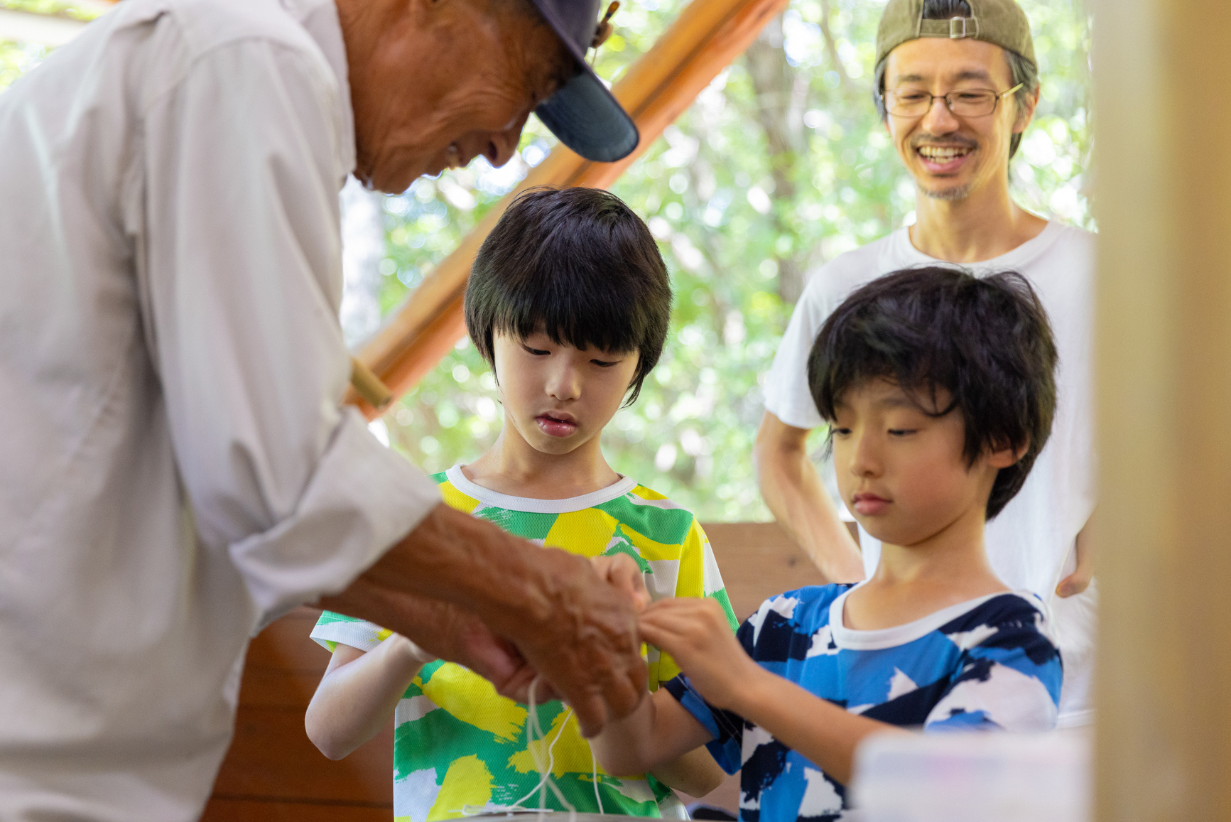 後ろで保護者に見守られながら二人でおもちゃ作りを教わるこどもたちの写真