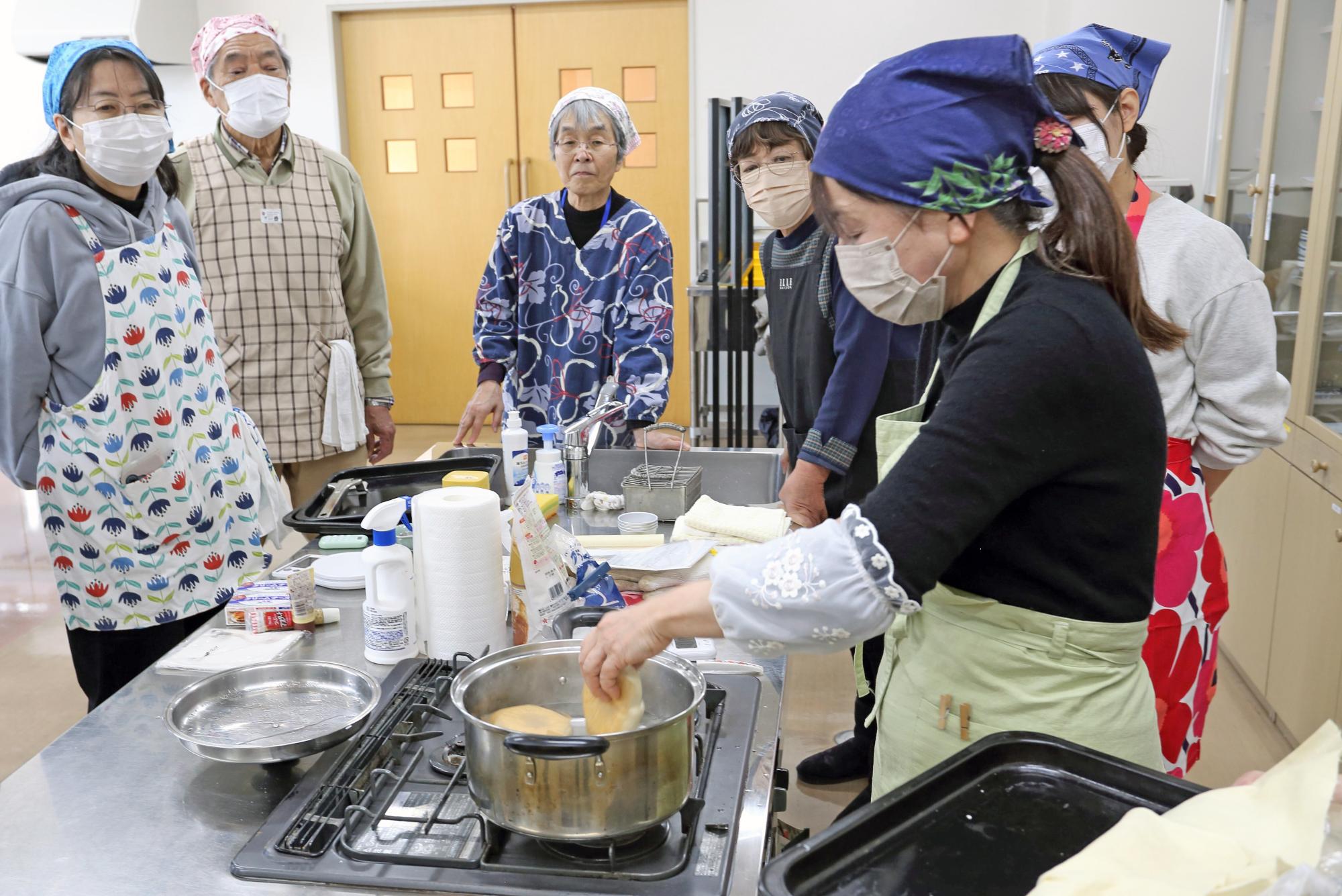 参加者たちがベーグルの記事を熱湯の入った鍋に投入する写真