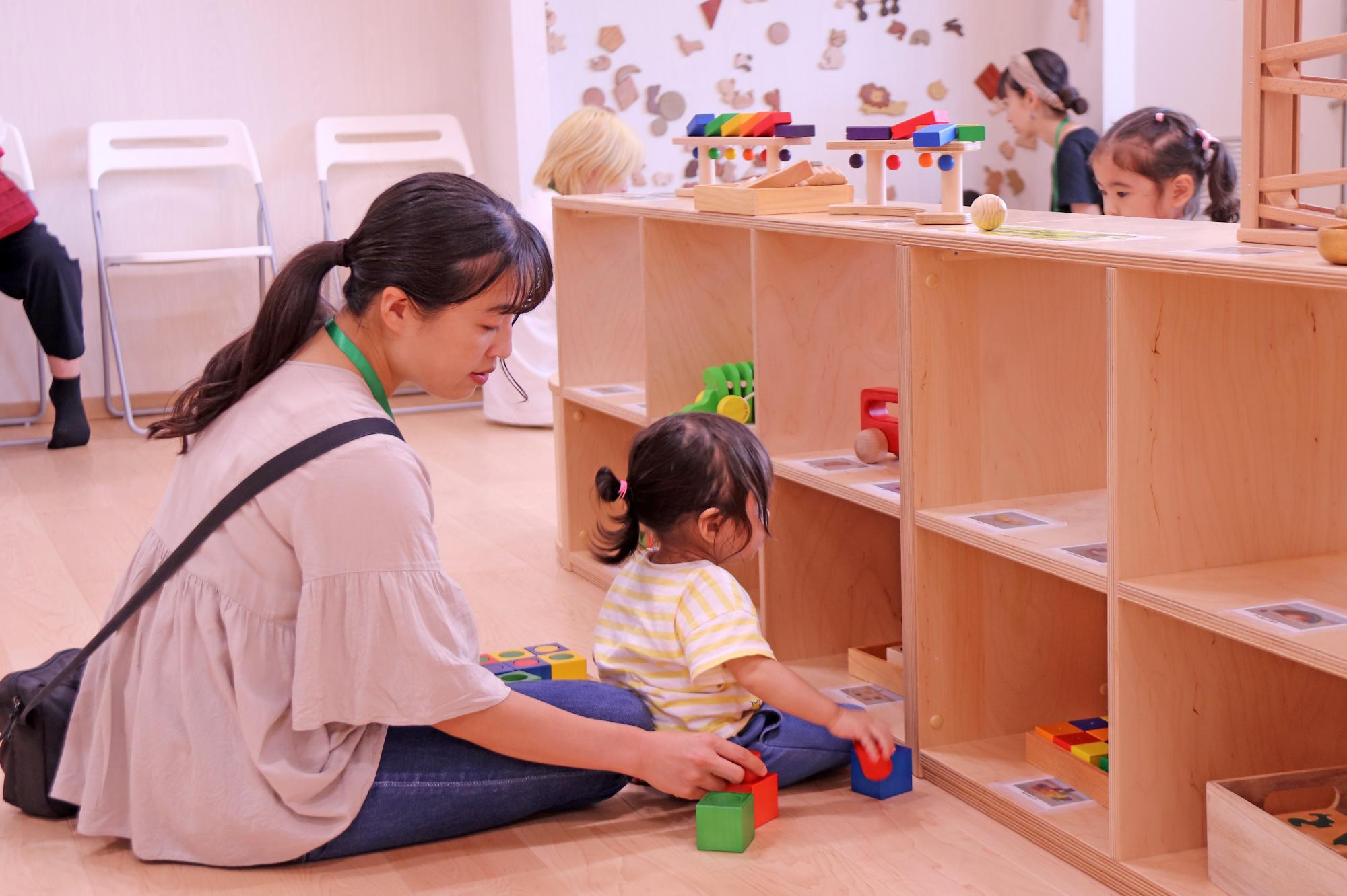 小さなお子さんと一緒に積み木のおもちゃで遊ぶ保護者の写真