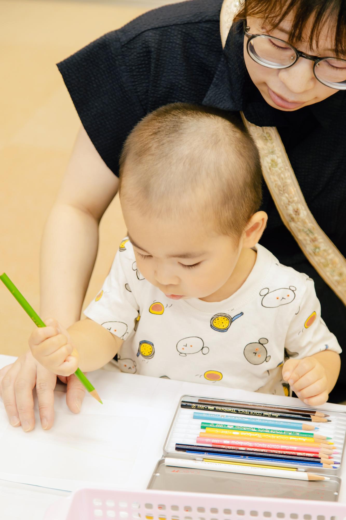 こどもがお母さんと一緒に色鉛筆でイラストを描いている様子の写真