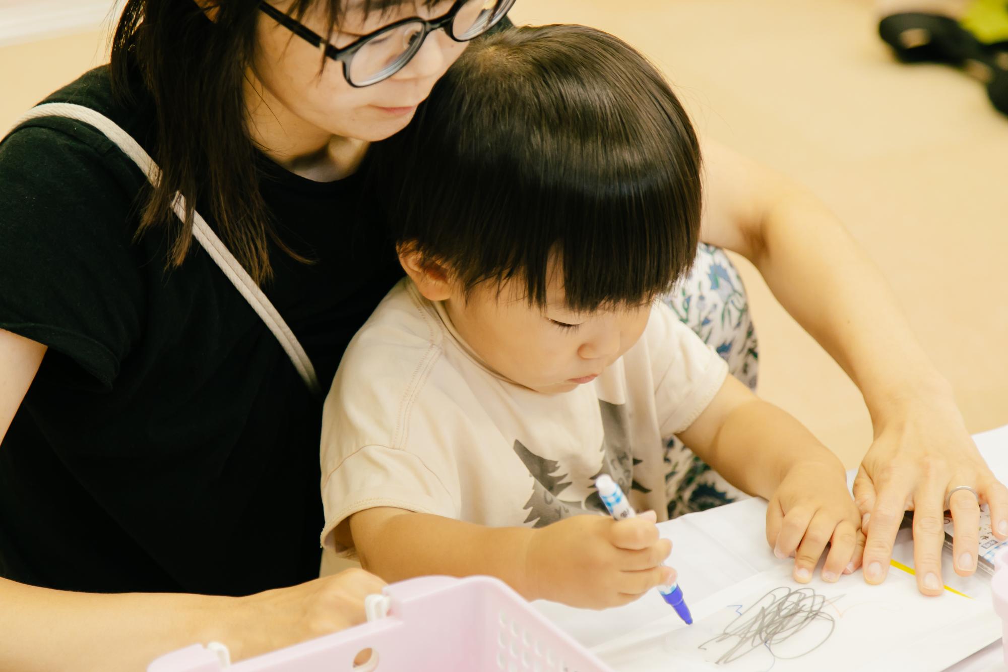 こどもがお母さんと一緒に色鉛筆でイラストを描いている様子の写真その1