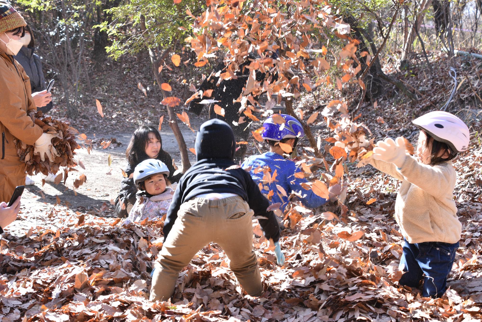 子どもたちが落ち葉をすくって散らしている写真