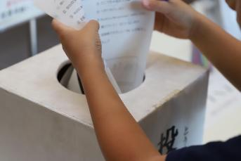 投票箱に投票用紙を入れる子どもの写真