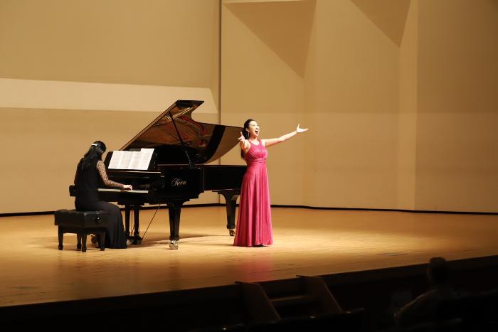 ステージ上でピアノの伴奏とともに歌う福井さんの写真