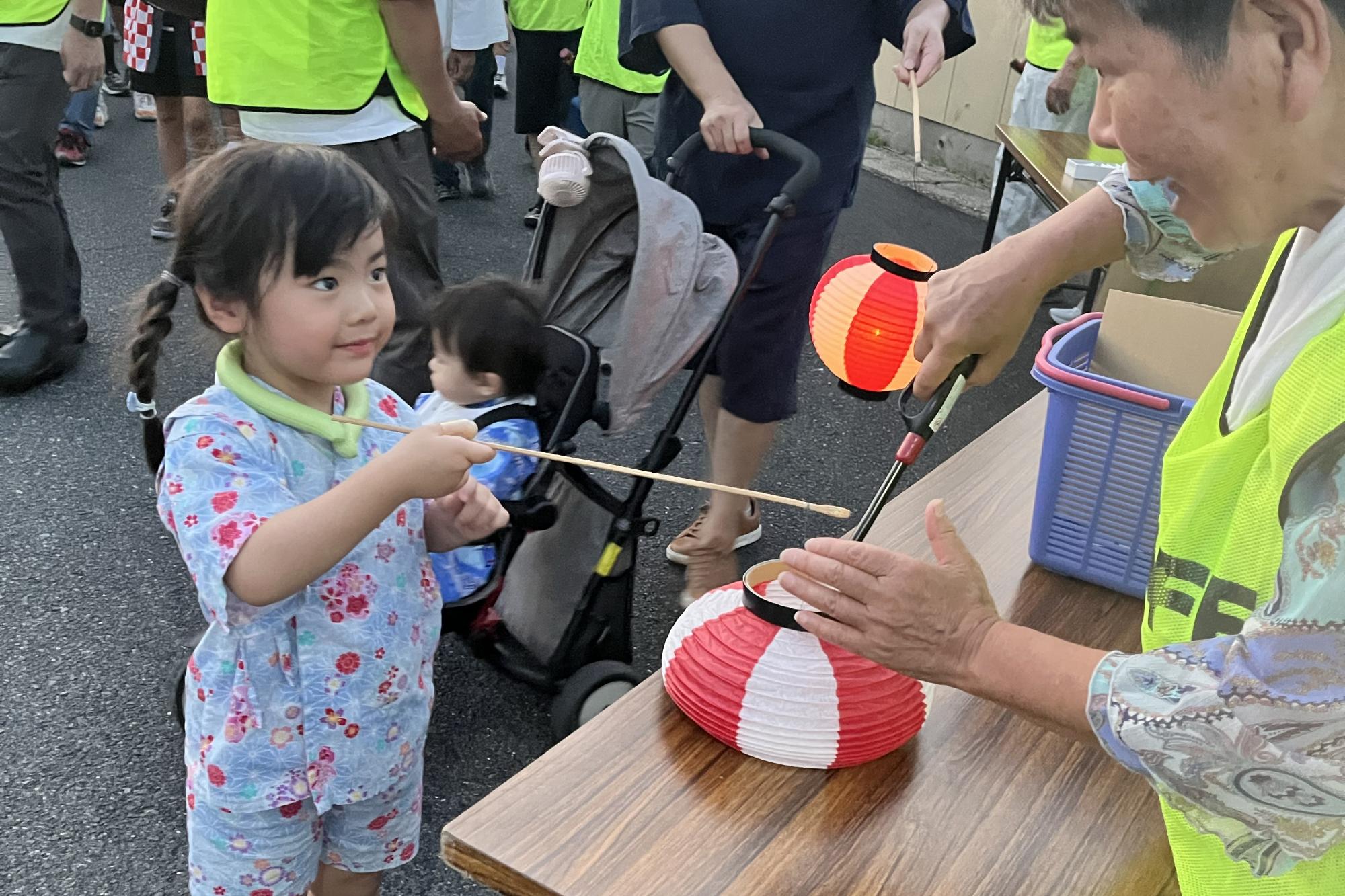 提灯に灯を灯してもらう女の子の写真