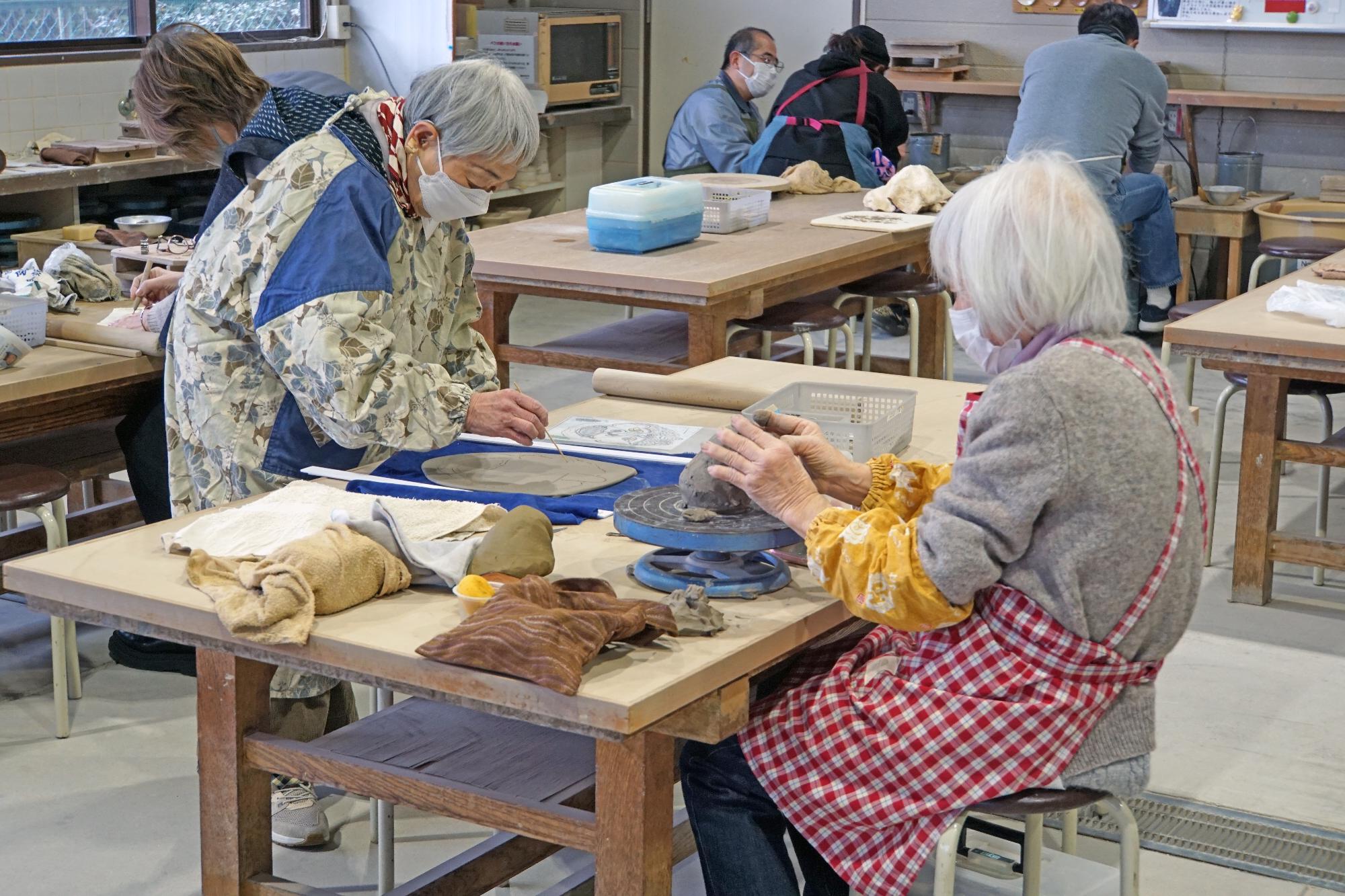 参加者が粘土に木の棒で模様を描いたり手でこねたりして作品を作っている写真