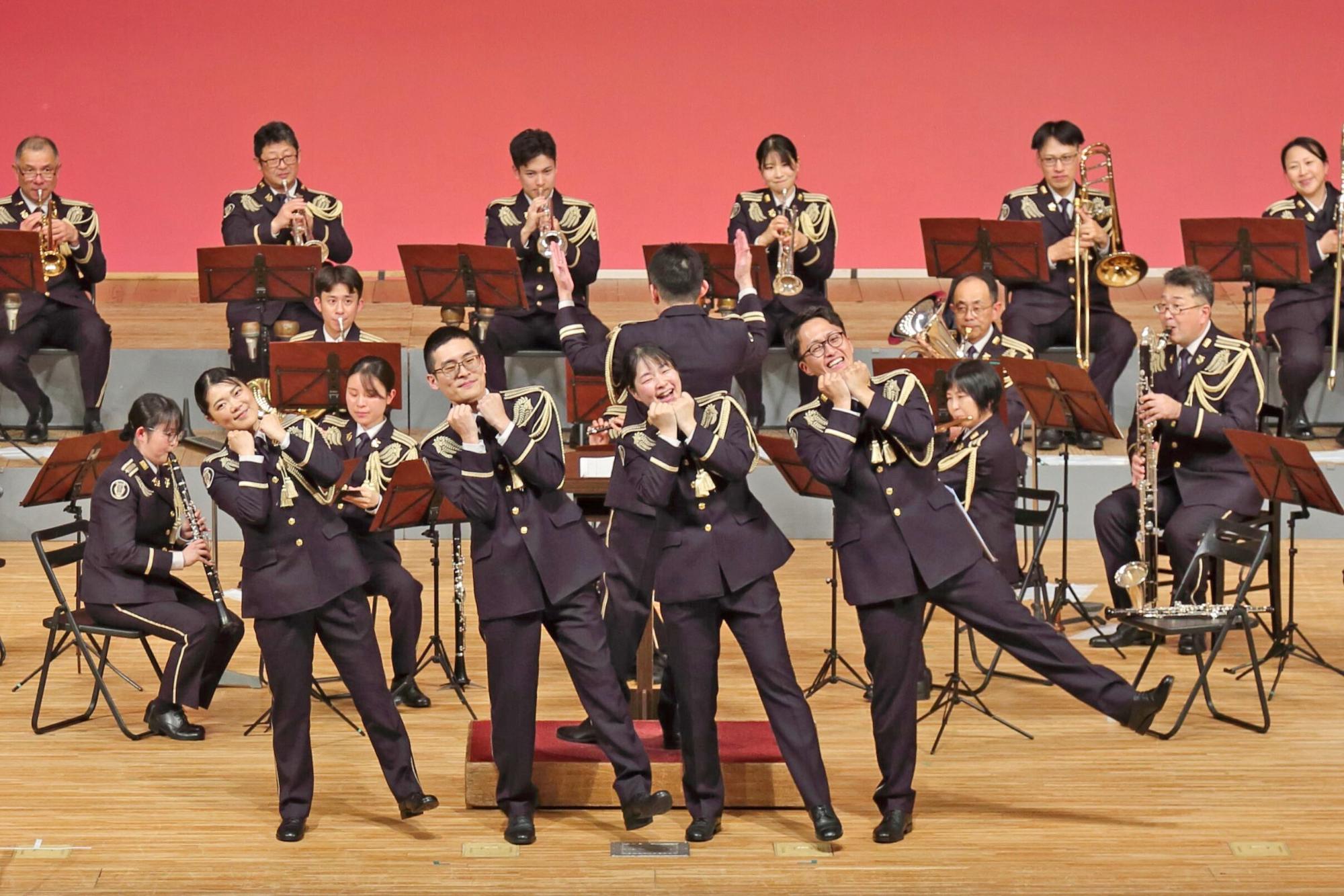 ステージ上で演奏を行う音楽隊とその前でダンスを披露する音楽隊の写真