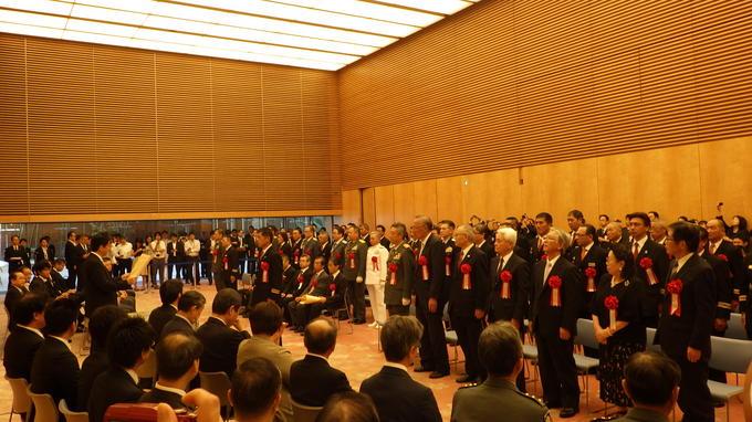 賞状を読み上げる安倍総理の前で起立し整列している受賞者の写真