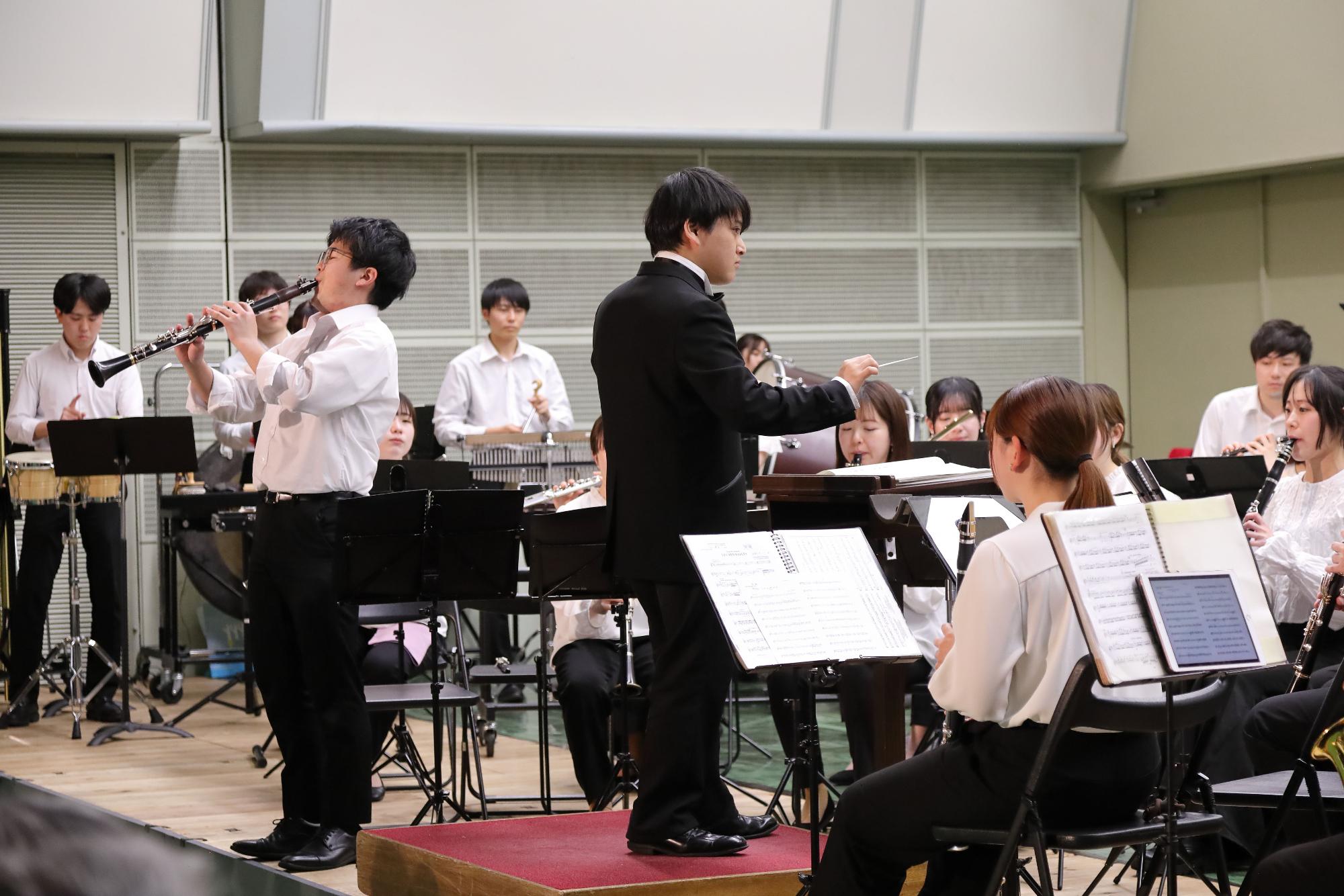 クラリネットのソロ演奏をしている男性と一致団結して演奏している団員の写真