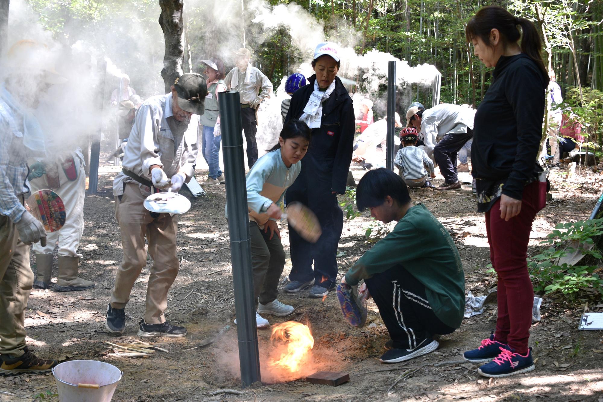 手作りの竹炭に火をおこすために一生懸命うちわであおぐ参加者たちの写真