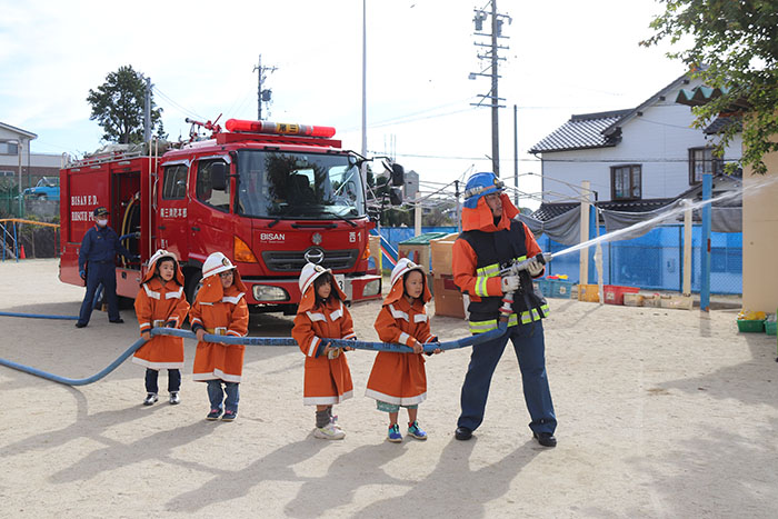 消防服に身を包み、ホースを手に持ち放水体験を行う園児たち