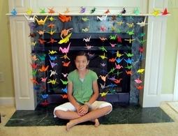 たくさんの折鶴の前に座り笑顔の折鶴計画の中心となった小学生の女児の写真