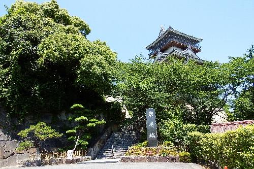緑に覆われた岩崎城正門と木々の上に見える天守閣の写真