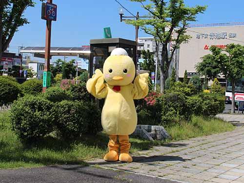 赤池駅のロータリーに立つ、ヘルピーの着ぐるみがポーズをとっている写真