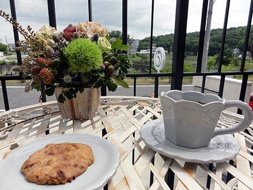 テーブルに花が飾られたカフェのテラス席でのクッキーとコーヒの写真