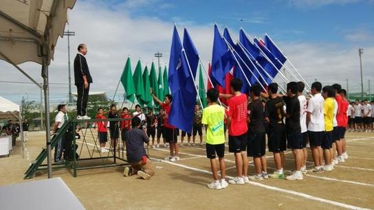 栄徳高等学校にて旗を持った生徒たちの前で壇上にたっている男性の写真