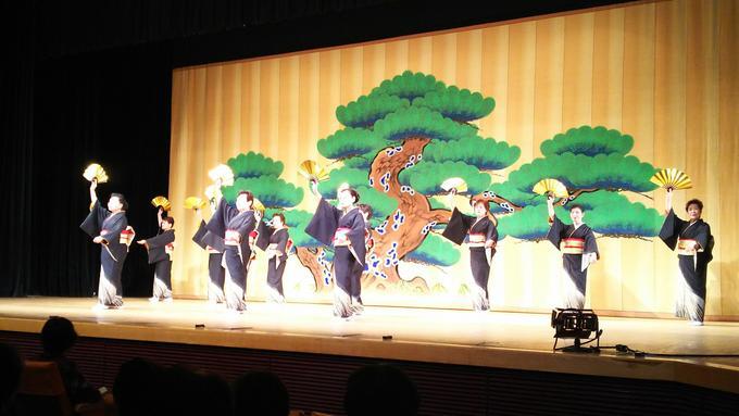 日本民踊研究会・おどる5市町の会主催の民踊お国めぐりにて壇上より団体で舞を披露する様子の写真