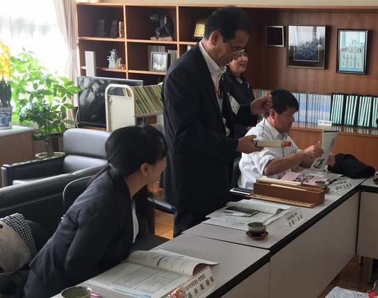 教育長と藤井委員が北小学校を訪問し席を立って話をしている男性の横でのぞき込んでいる女性の写真