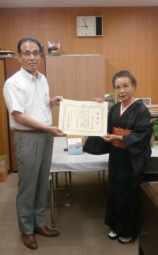 川田きし江様より市内小中学校へ、ご自身の執筆された図書を寄贈した際に賞状を持った右に女性、左に男性の写真