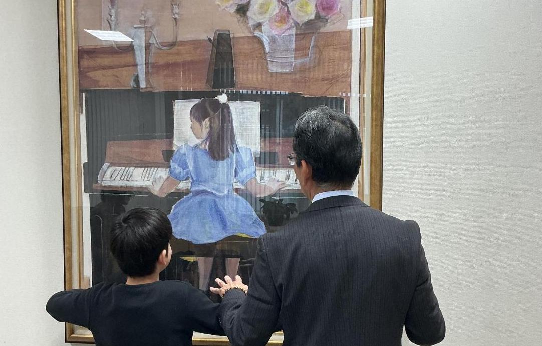 絵画のようにビアノを弾く真似をする児童と教育長