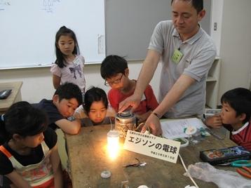 発明クラブ4年生Aクラスの子供たちが指導を受けながらエジソンの電球作成をしている写真